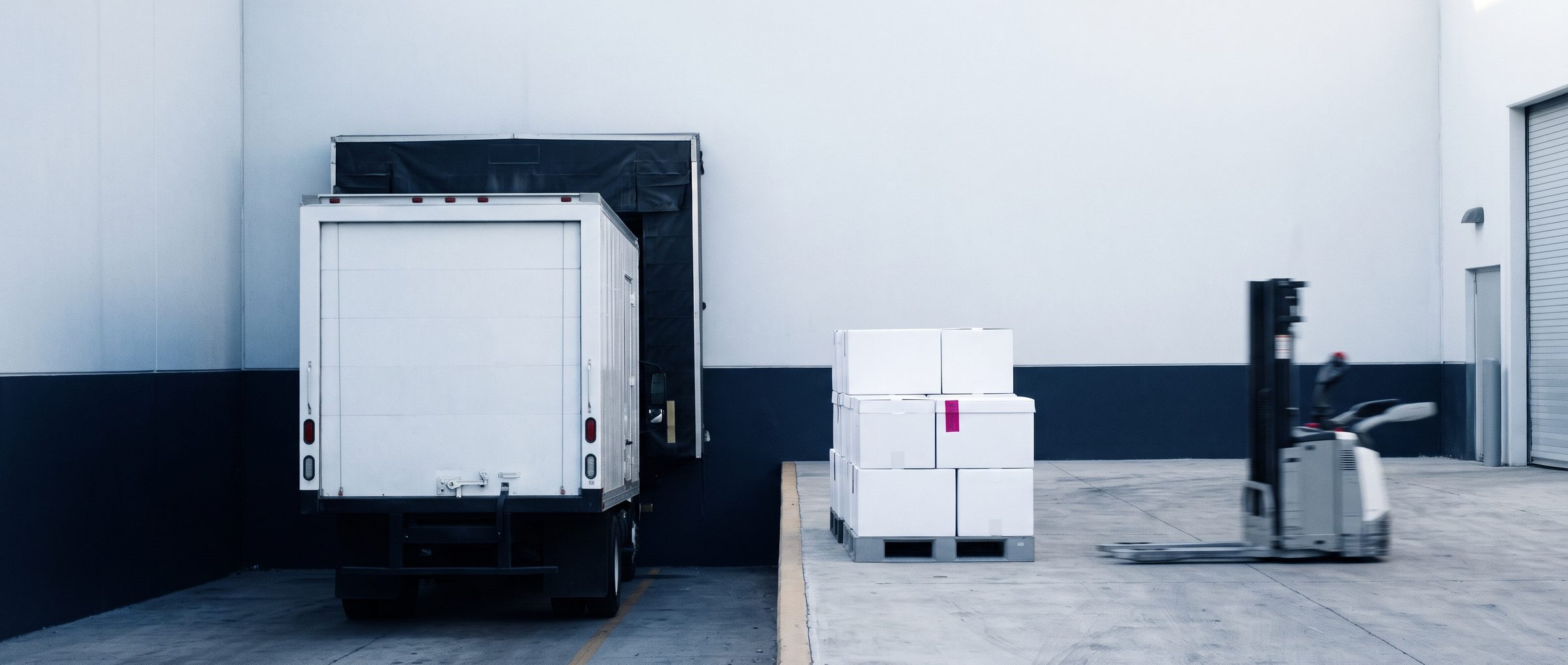 Camión refrigerado en un andén farmacéutico con un palet de cajas térmicas y un patín eléctrico en movimiento.